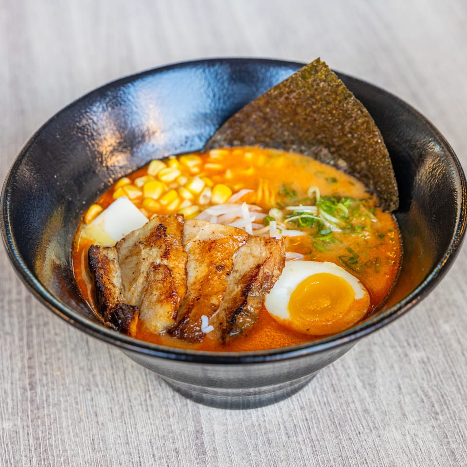 A bowl of Ramen Kenjo's ramen with pork, corn, egg, and seaweed in a rich broth.
