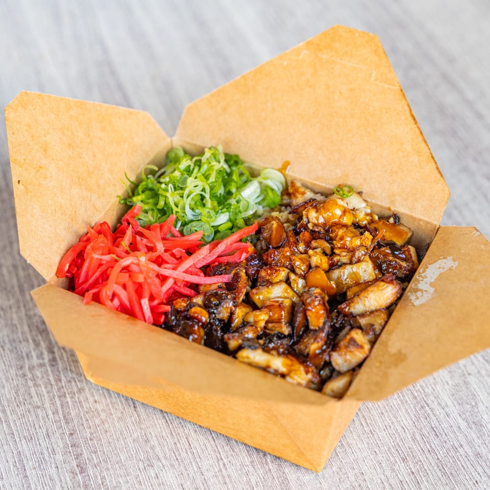 Ramen Kenjo's Japanese chashu donburi with pickled ginger and green onions in a takeout box.