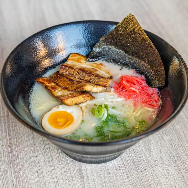A black bowl of Ramen Kenjo's ramen with pork belly, egg, seaweed, and red ginger.