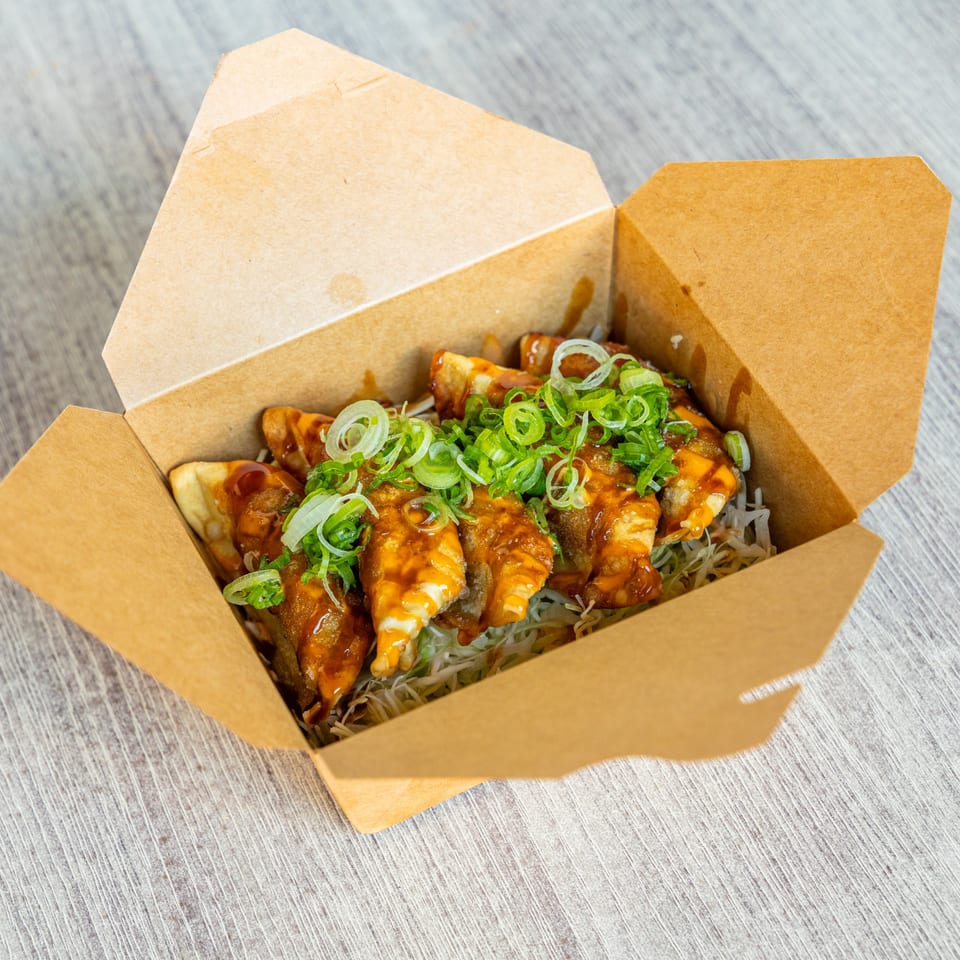 Ramen Kenjo's Japanese gyoza dumplings with sauce and green onions in a takeout box.