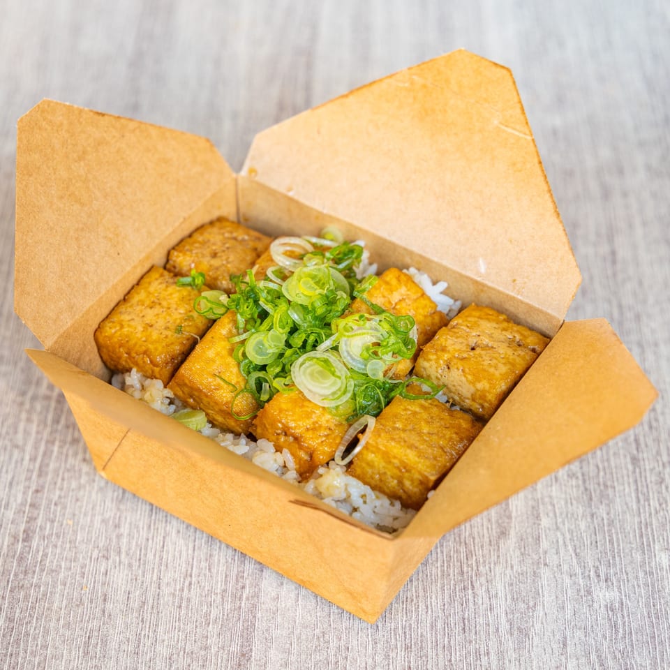 Japanese tofu and rice dish with green onions in a brown takeout box.