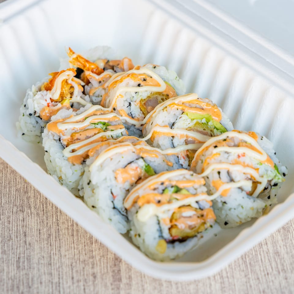 Sushi rolls with white and orange sauce in a white takeout container from Ramen Kenjo.